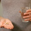 A woman holding pills in one hand and a glass of water in the other.