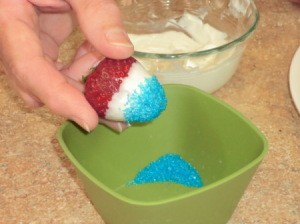 Dipping chocolate dipped strawberries into blue sprinkles.