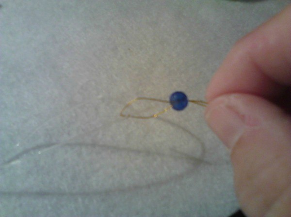 Folded wire and elastic being pulled through a bead.
