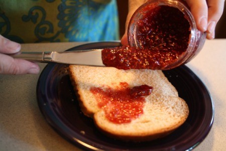 Homemade raspberry jam being spread on a piece of bread