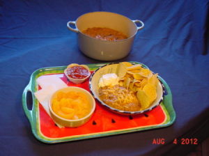 Tray of food on blue background with Dutch oven in background of frame.