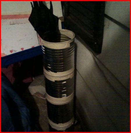 Large tin cans taped together to make an umbrella stand.