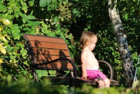 Little girl sitting quietly on a bench, in the garden.