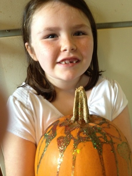 Little girl holding glitter decorated pumpkin.