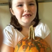 Little girl holding glitter decorated pumpkin.