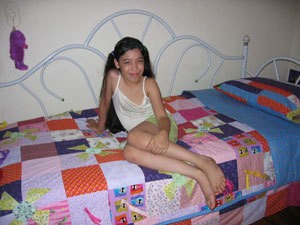 Young girl sitting on her bed with birthday quilt.