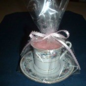 Cup and saucer candle wrapped in clear paper and tied with a pink bow.