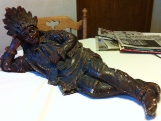 Statue of Native American lying on side with head propped up on hand.