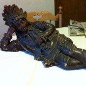 Statue of Native American lying on side with head propped up on hand.