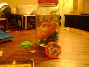 Side view of jar with toys inside and next to it on table.