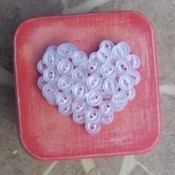 Pink box with white buttons arranged in the shape of a heart.
