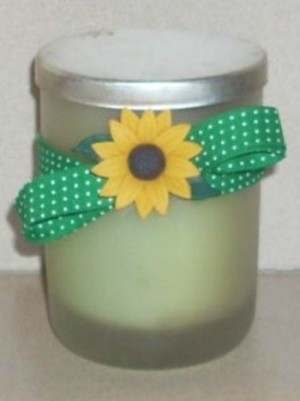 A container of bath salts with a sunflower button and green ribbon.