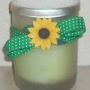 A container of bath salts with a sunflower button and green ribbon.