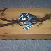 Bench decorated with a painted raccoon hanging onto a branch.