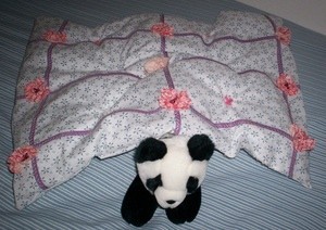 A small quilt covering a stuffed panda.