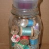 Candle holder on top of jar filled with spools of thread.