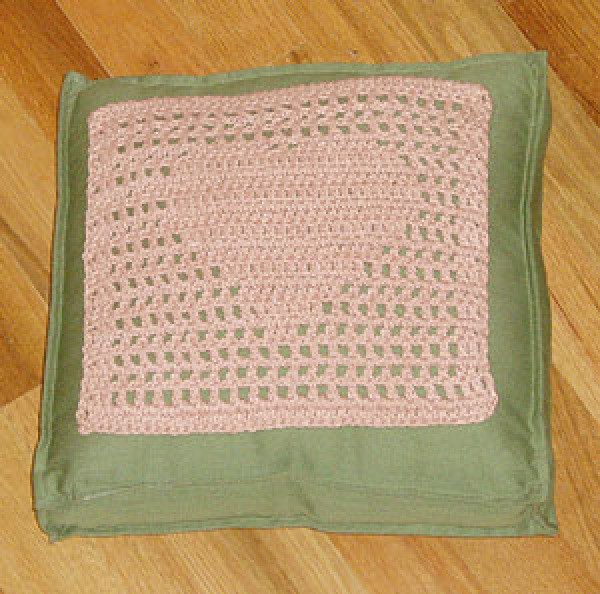 Pink filet crochet heart square on green pillow.
