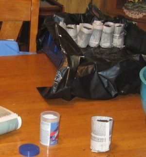 Gardening: Paper Pots - making the pots with completed ones in a plastic bag lined container in the background, closeup