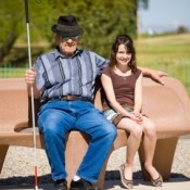 a blind man and a girl sitting on a bench