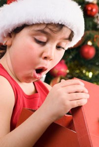 A child opening a box in front of a Christmas tree.