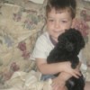 A small boy holding a black toy poodle.