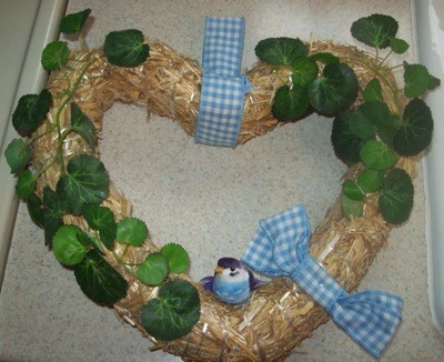 Straw wreath with green artificial leaves and ribbons.