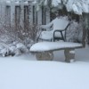 Snow covered garden chair, bench, and ground.