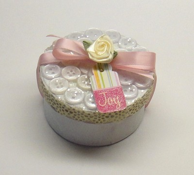 Round box decorated with buttons and pink ribbon.