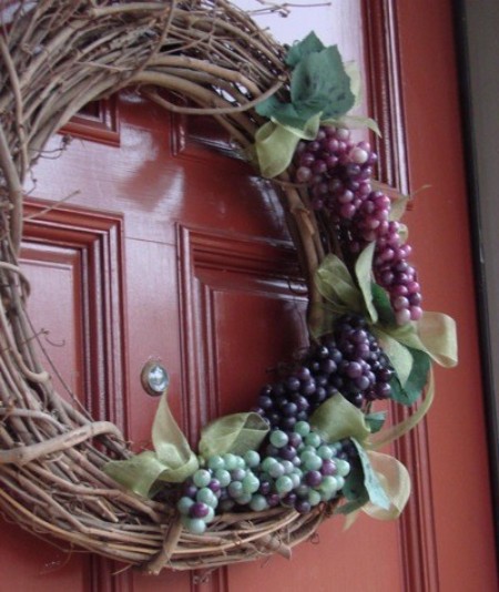 A grapevine wreath decorated with artificial grapes and leaves.