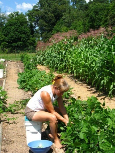 A woman sitting on a covered bucket while weeding in the garden.