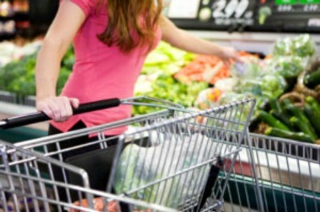 Woman and grocery shopping cart in produce aisle.