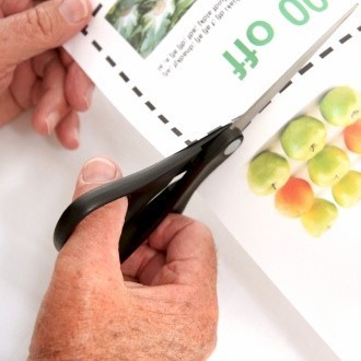 Scissors cutting out a coupon from a sheet of paper.
