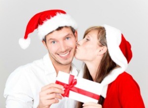 A woman kissing her boyfriend and giving him an envelope with homemade coupons in it.