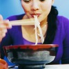 An Asian lady eating the frugal meal of ramen noodles.