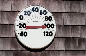 A thermometer on the side of a house reading 100 degrees fahrenheit.