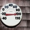 A thermometer on the side of a house reading 100 degrees fahrenheit.