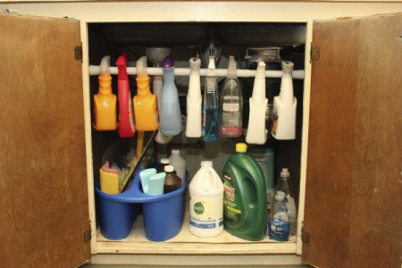 Spray bottles hanging on bar under sink.