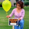 A woman putting a balloon on a garage sale sign.