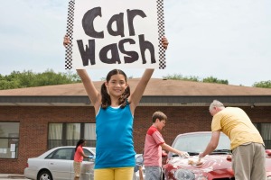A girl holding up a car wash sign at a school fundraiser.
