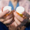 Old woman holding prescription drug bottles.