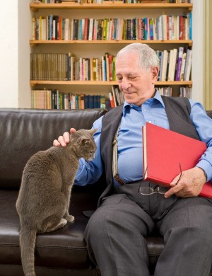 An old man sitting on a couch with his cat.