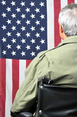 Disabled veteran in a wheelchair in front of an American flag.