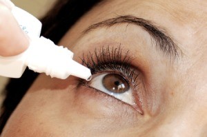 Woman with puffy eyes using eye drops.