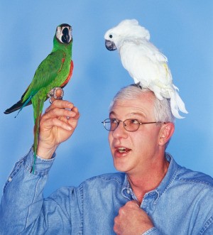 Birds perched on a man's hand and shoulder.