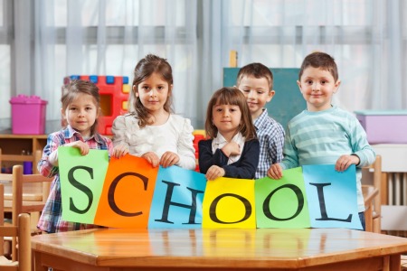 Preschool kids sitting at a table holding a sign that says school.