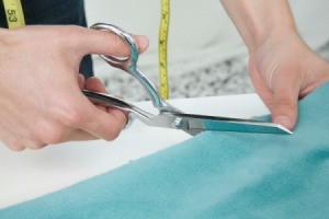 Someone cutting light blue fabric with scissors.