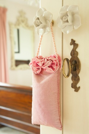 A pink bag filled with potpourri hanging from a door handle.