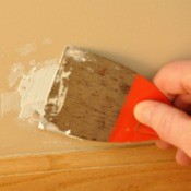 Applying putty to a damaged portion of a painted wall.