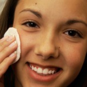 A girl looking in the mirror and using a medicated pad to treat acne.
