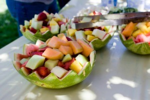 Fruit salad bowls made in carved out watermelons at a large outdoor birthday party.